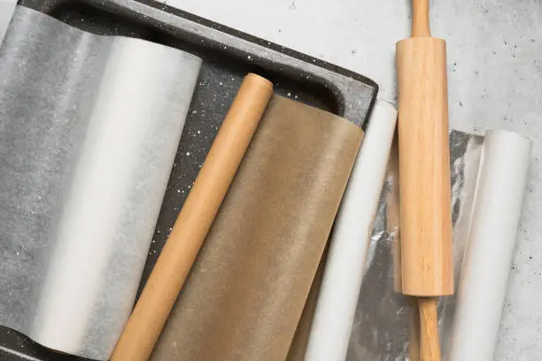 Photo of Different type of paper for baking needs. Parchment paper, foil, wax paper close up on grey stone background, flat lay