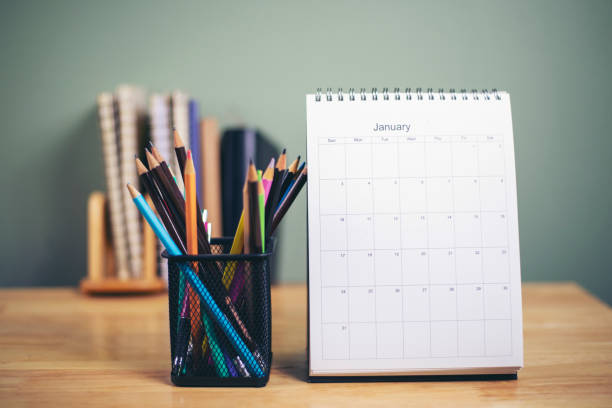 istock Desk for student education concept. Book, and pencil for study for exam. Calendar placed on white School table with bookshelf and green wall background for student plan to work at home. 1350754711