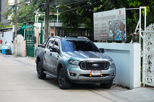 Gray silver colored Ford Ranger parked in front of wall in street of Bangkok, at right side is a billboard banner
