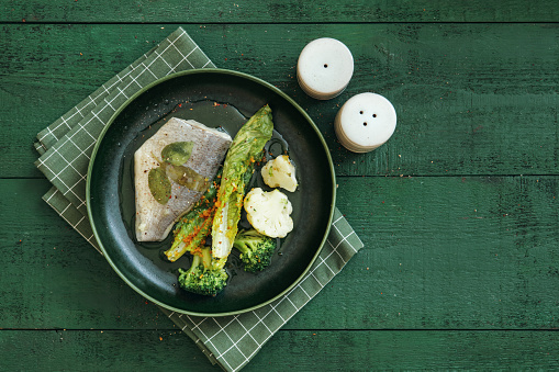 Snapper with basil-mint sauce and steamed vegetables. Flat lay top-down composition on dark green background.