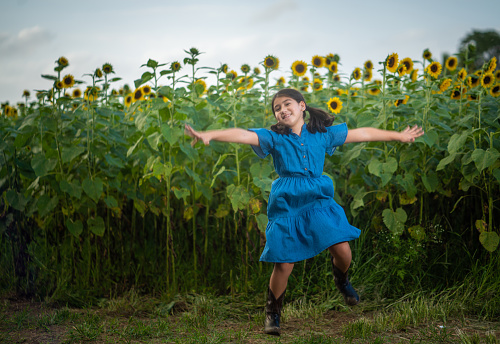 Little hispanic girl wearing a blue denim dress playing around in a sunflower field