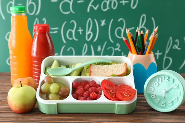 Lunch box with appetizing food and alarm clock on table near chalkboard stock photo