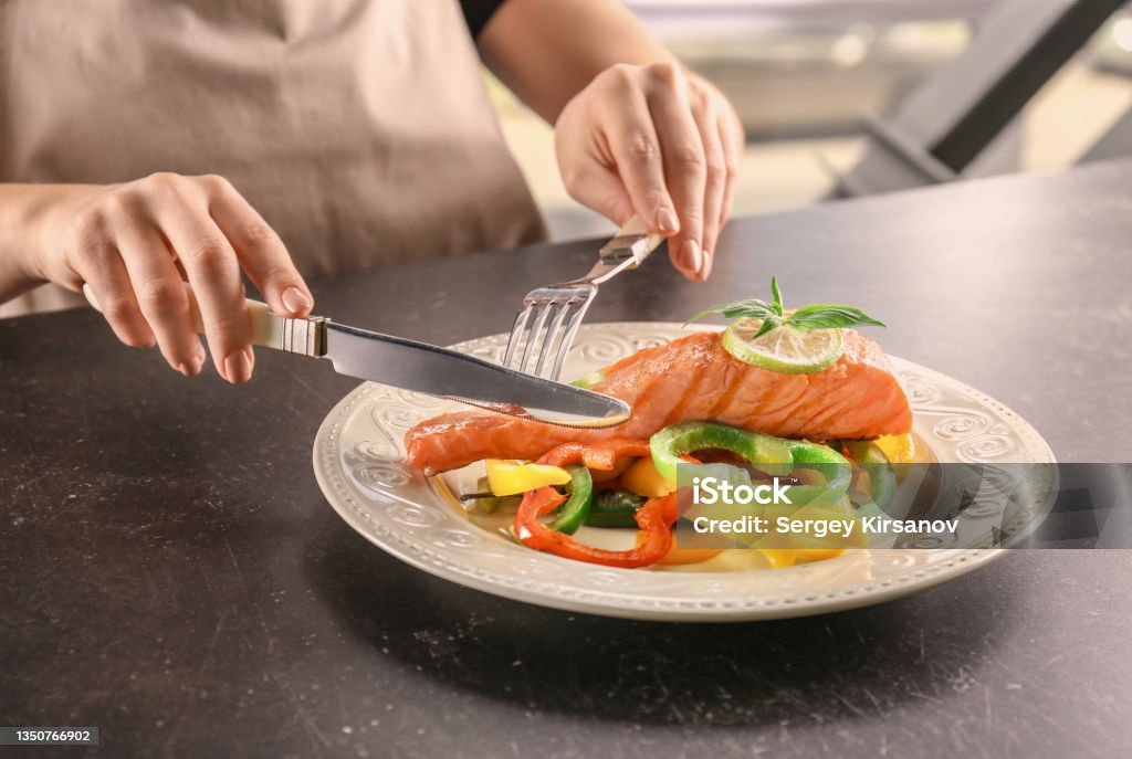 Woman eating tasty salmon with fresh peppers at table Eating Stock Photo