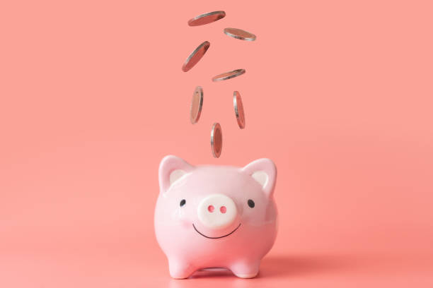 Coins falling into pink piggy bank on pink background with copy space. Financial and saving money concept. stock photo