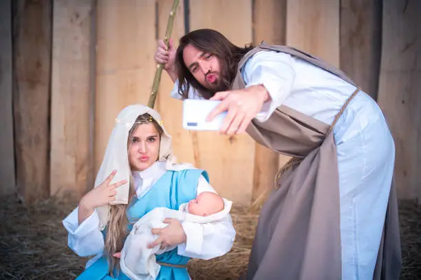 Biblical characters of the virgin mary and joseph taking a selfie while joking in a crib