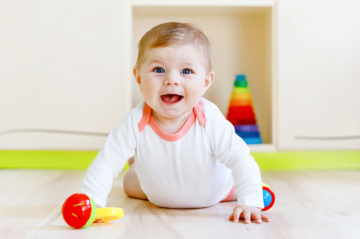 Cute happy smiling baby playing with colorful rattle toys. New born child, little girl looking at the camera and crawling. Family, new life, childhood, beginning concept. Baby learning grab