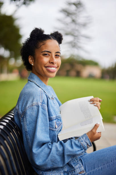 istock Smiling young college student reading a book on a campus bench 1350779325