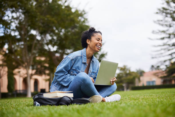 istock Female university student laughing while working on a laptop on a campus lawn 1350779584