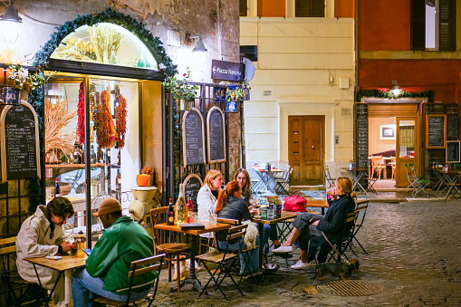 Rome, Italy, October 28 -- Some customers enjoy life and the Italian cuisine sitting outside a lovely restaurant and bistro along Via dei Coronari, near Piazza Navona, in the historic and baroque heart of the Eternal City. Called Via Recta in medieval times, Via dei Coronari is still today one of the main pedestrian routes to St. Peter's Basilica from the center of Rome and from the Piazza Navona area. The Rione Parione, the district surrounding Piazza Navona, is one of the most beautiful and visited districts of Rome for the presence of countless artistic and historical treasures, monuments and ancient Romanesque and Baroque churches, but also for its squares and alleys to explore freely, where it is easy to find typical restaurants, small artisan shops, street artists, and the original Roman soul. In 1980 the historic center of Rome was declared a World Heritage Site by Unesco. Image in high definition format.