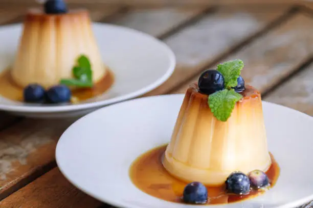 delicious flan with blueberries on white plate on wood