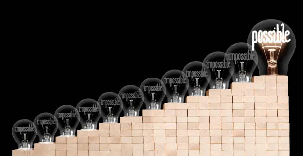 Large group of shining and dimmed light bulbs on wooden block ladder with fibers in a shape of Impossible and Possible words isolated on black background. Concept of Motivation, Success and Change