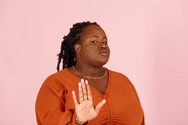 Serious black woman refuses offer showing Stop gesture on pink background stock photo