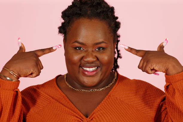 Funny black woman points to head with both hands finger on pink background stock photo