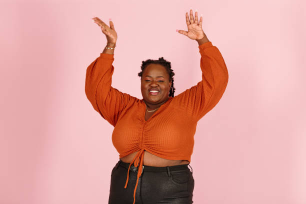 Excited young black plus size woman dances on pink background stock photo