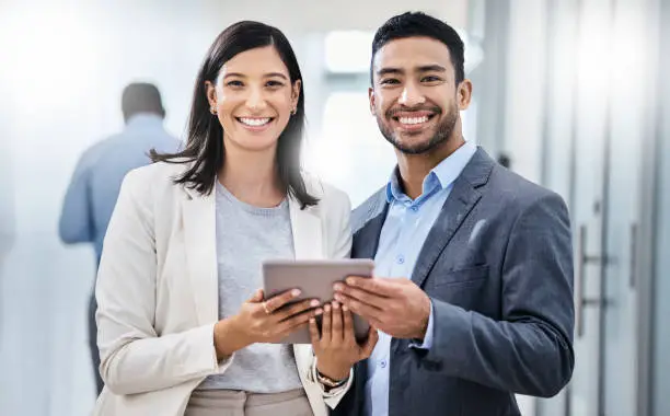 Photo of Shot of two businesspeople standing together and holding a digital tablet in an office
