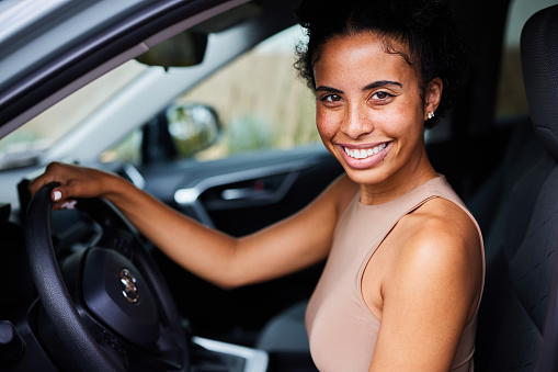 Portrait of a young woman smiling while sitting in the driver's seat of her car before going for a drive