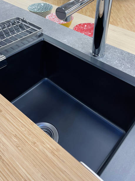 istock Image of modern kitchen with rectangular, black, synthetic single bowl sink with stainless steel top rails and bamboo chopping board, chrome monobloc mixer tap, grey granite countertop, elevated view 1350793590