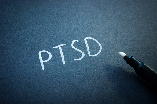 PTSD or Post Traumatic Stress Disorder handwritten on the black sheet of paper.