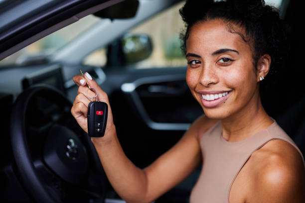 Smiling young woman holding keys while sitting in her car