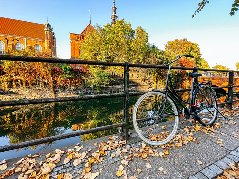 The heart of the old town of Gdansk in a sunny fall day. A bicycle on the embankment, strewn with fallen maple leaves. The old town hall (Ratusz Staromiejski) on the background.