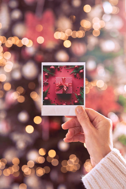 istock Female hand holding Christmas card with gift on xmas tree background. 1350795190
