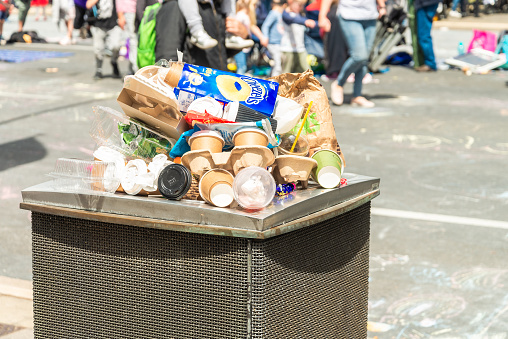 Adelaide, Australia - November 9, 2019: Overflowing rubbish bin during the street carnaval on a day while people walking by in the background