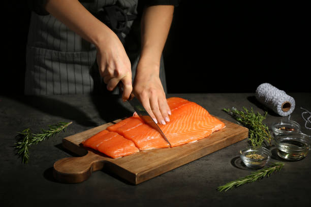 Woman cutting fillet of fresh salmon at table stock photo