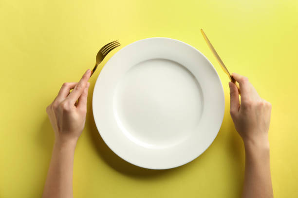 Female hands with cutlery and empty plate on color background stock photo