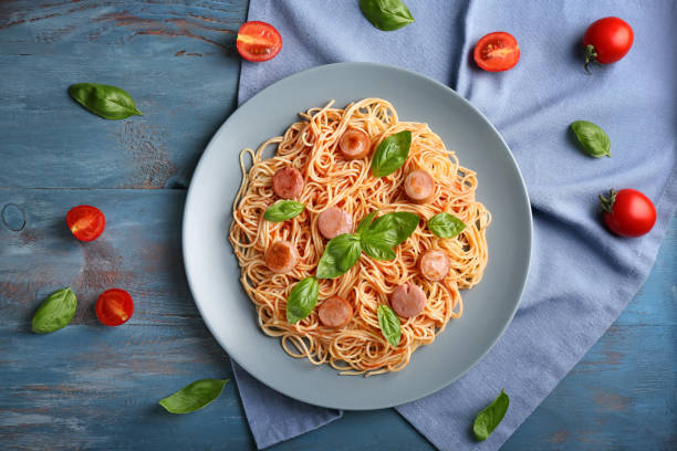 Plate with delicious pasta and sausage on color wooden table stock photo