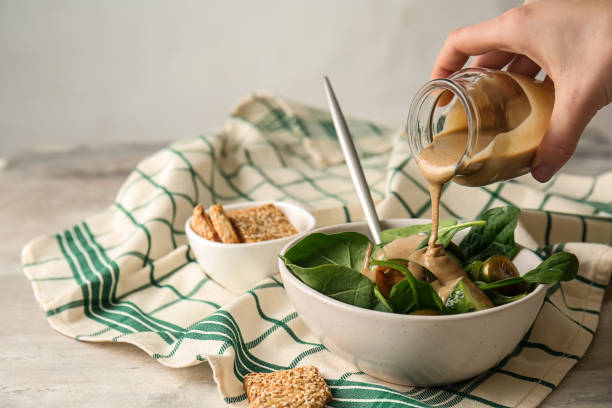 wylewanie smacznego tahini ze słoika na świeże warzywa w misce - condiment zdjęcia i obrazy z banku zdjęć