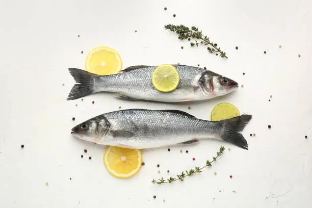 Photo of Tasty fresh seabass fish with spices on white background