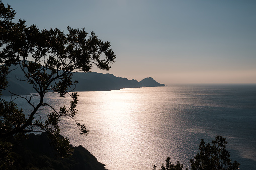 Capu Rossu headland on the west coast of Corsica silhoutted against the Mediterranean sea shimmering in the late afternoon sunshine