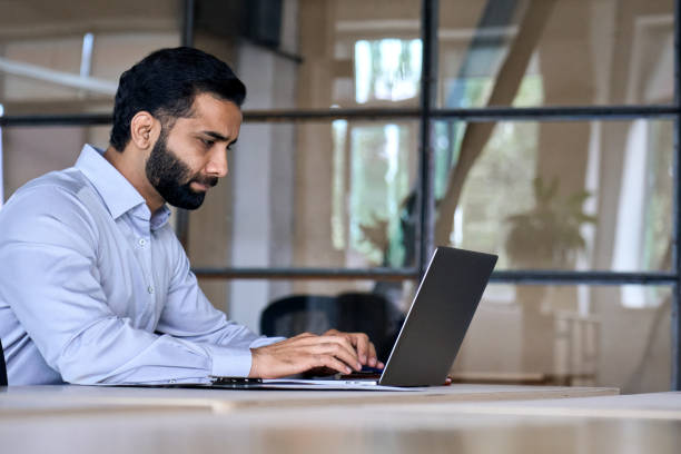 istock Serious ethnic latin Indian businessman working in modern office using laptop. 1350800586