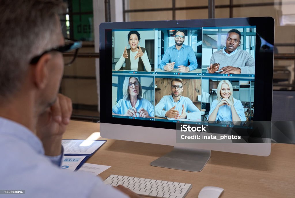 Businessman talking with team leading virtual meeting on computer. Over shoulder Business man talking with diverse team people having digital group video call global conference working leading online virtual meeting training on pc computer. Over shoulder videocall screen view Education Training Class Stock Photo