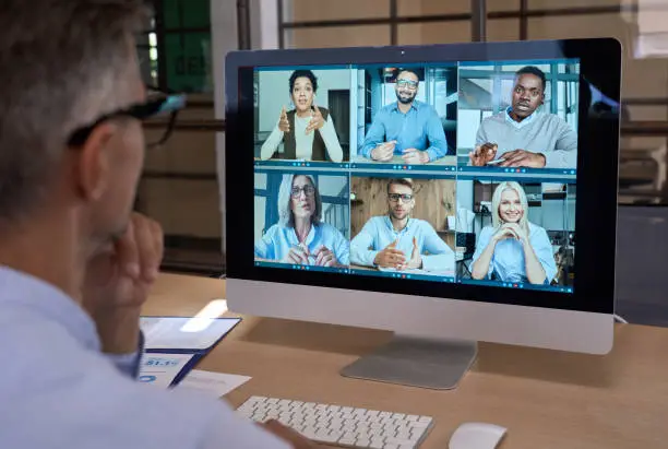 Photo of Businessman talking with team leading virtual meeting on computer. Over shoulder