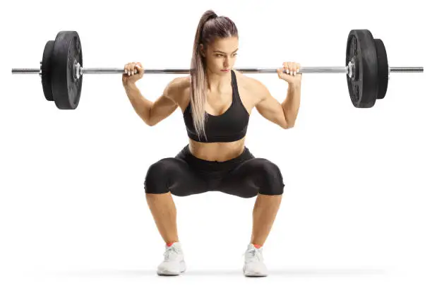 Fit young woman bodybuilder kneeling with heavy weights isolated on white background