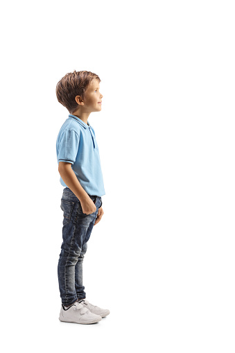 Full length profile shot of a boy in a blue t-shirt standing and watching something isolated on white background