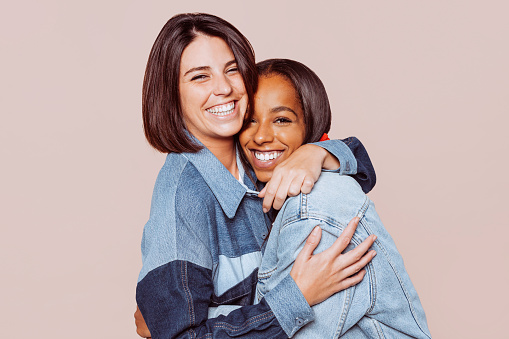 Dos alegres chicas multinacionales abrazándose y sonriendo juntas ante la cámara photo