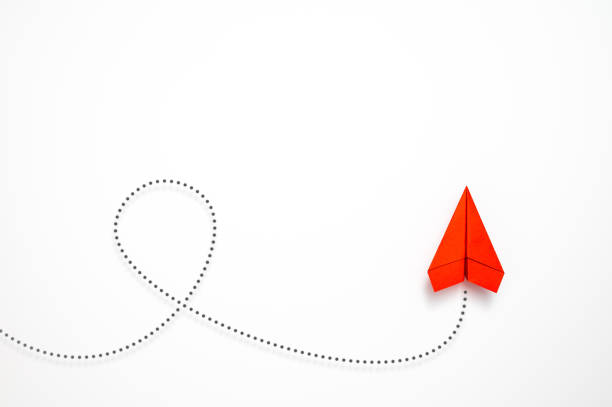 Red paper plane with dotted contrail flying a loop against white background. Table top view, flat lay, copy space.