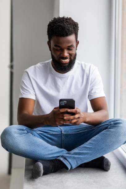 istock Handsome african man sits home on windowsill, reads text messages, sends email, uses his phone and fast internet connection. 1350808841