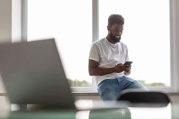 istock Smiling African American man sit at home kitchen office text message on smartphone online. 1350809638