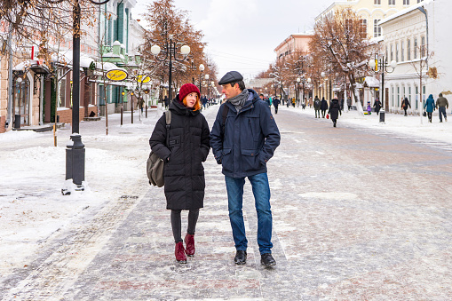 Tourists man and woman walking along city street in winter cloudy day. People spending winter weekend in city. Father and daughter wearing winter casual clothes. Urban vacation concept.