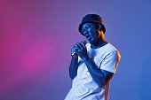 Studio shot of emotive african man with microphone isolated over gradient purple pink color studio background in neon filter