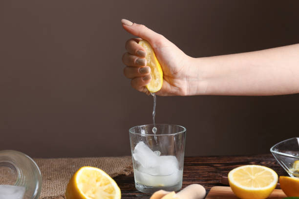 Woman squeezing lemon juice into glass with ice on table stock photo