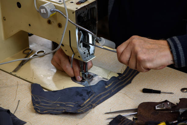 istock Hands of repairman fixing problems with professional industrial sewing machine in shoemaker workshop. Testing of machine stitching. Selective focus. 1350813039