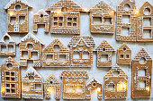 Image of rows of homemade, house-shaped, gingerbread biscuits, cookies iced with white glace icing illuminated by fairy lights, Christmas village display, marble effect background, elevated view
