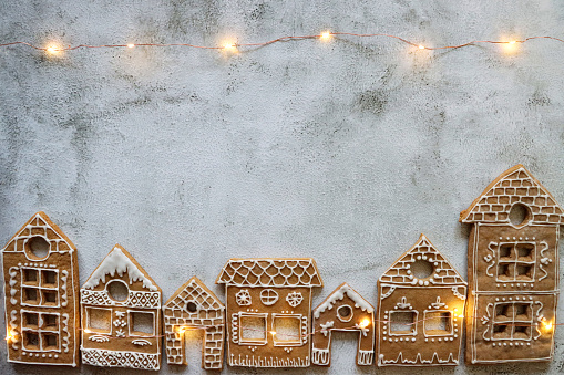 Stock photo showing elevated view of freshly prepared, homemade house-shaped gingerbread cookies decorated with white, glace icing forming a Christmas village themed party food idea.