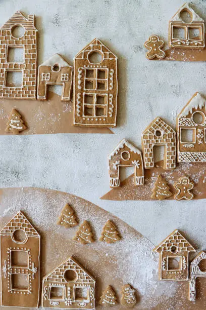 Photo of Image of Christmas mountain village display of homemade, house-shaped, gingerbread biscuits, Christmas trees, snowman and gingerbread men cookies iced with white glace icing, marble effect background, elevated view