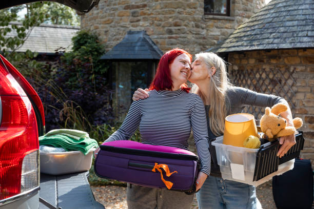 I Miss You Already Woman in the North East of England packing up her parents car with her mothers help while she prepares to move cities to attend university. They are standing together holding belongings while the mother kisses her daughters cheek. northern europe family car stock pictures, royalty-free photos & images