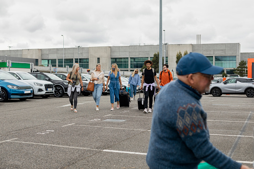A group of friends has landed at the airport and they are walking in the car park ready to load the car trunk with their luggage.